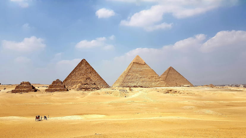 The great pyramids of Egypt during the day time from afar. A small group of people walking with a caravan.
